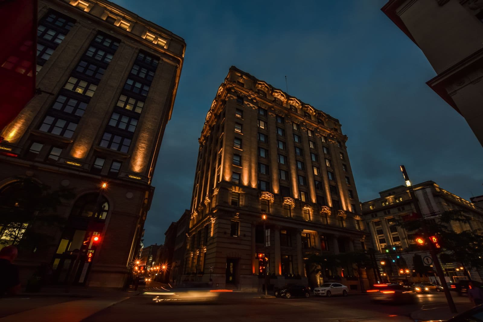 Un carrefour du Vieux-Montréal à la tombée du jour, façades éclairées et traînées de phares.
