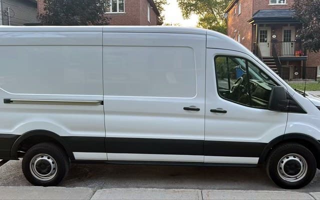 La fourgonnette Ford Transit de TractoPlus, blanche, vue de profil dans une rue résidentielle.